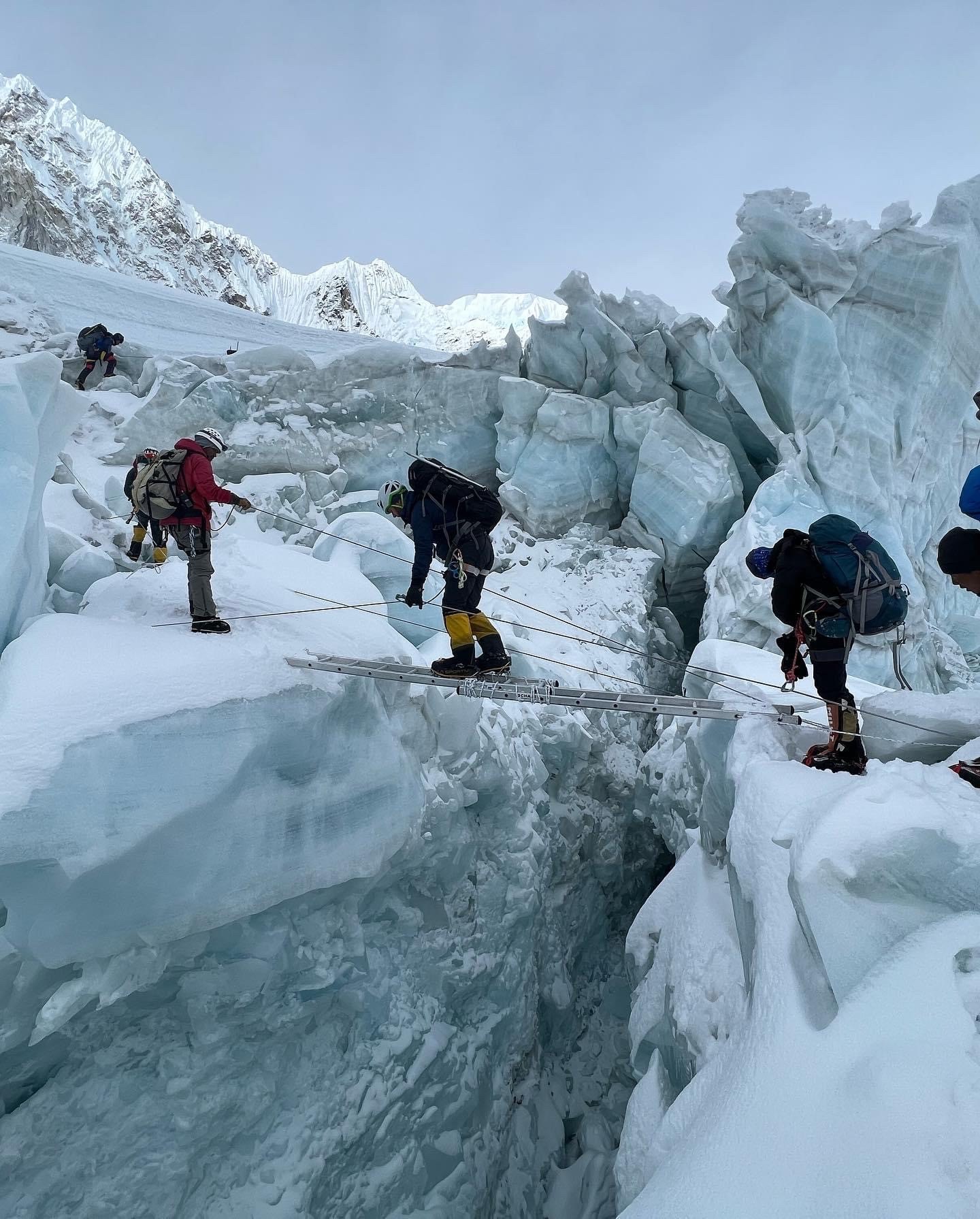 Climbers cross over a crevasse in the Himlayas, inching along a ladder.